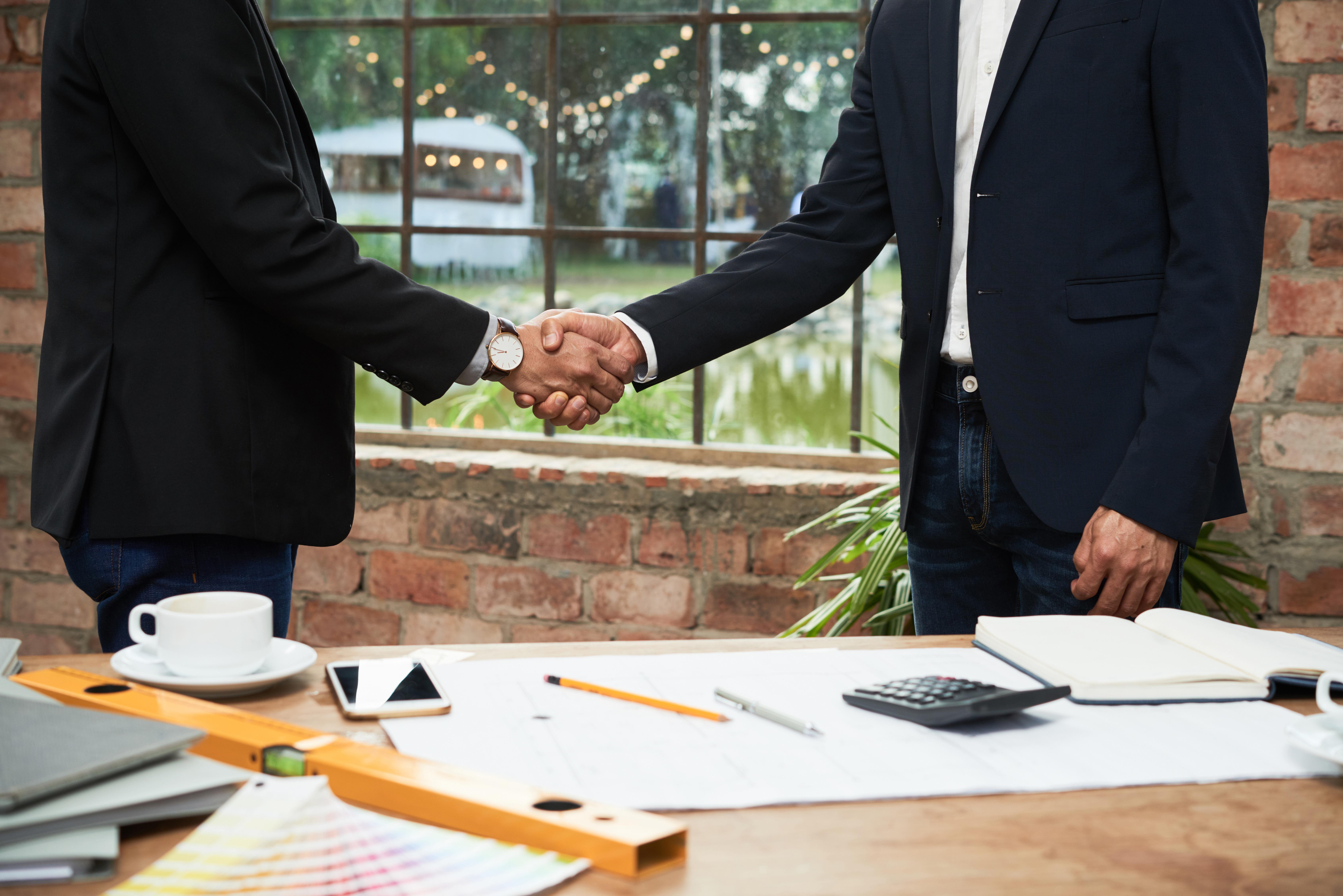 Two professionals shaking hands over a pile of documents