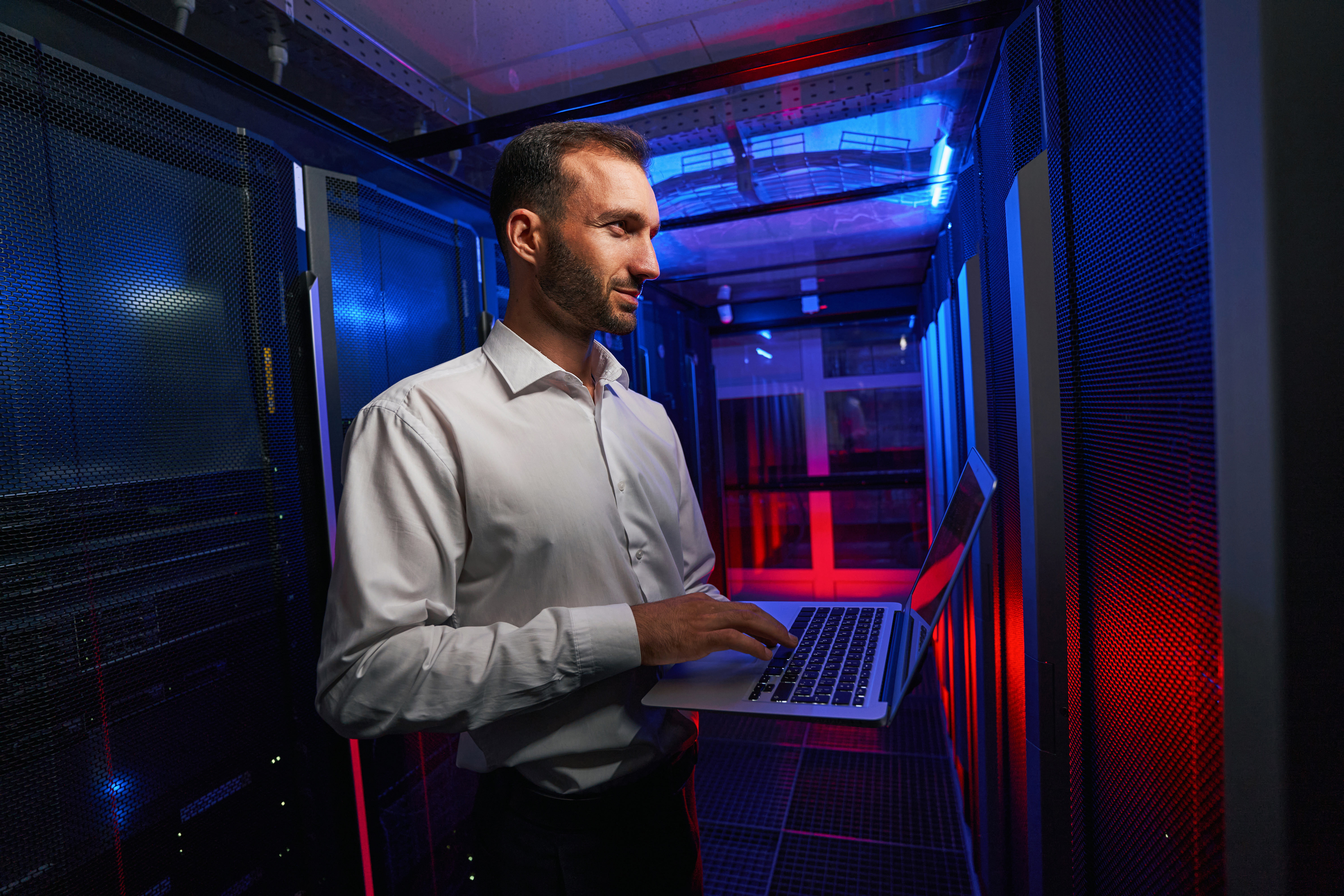 An IT professional standing in front of servers holding a laptop